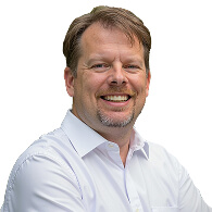 A middle-aged man with light brown hair and a goatee is smiling, wearing a white collared shirt and standing against a plain white background, representing Memcyco at RSA Conference 2025.